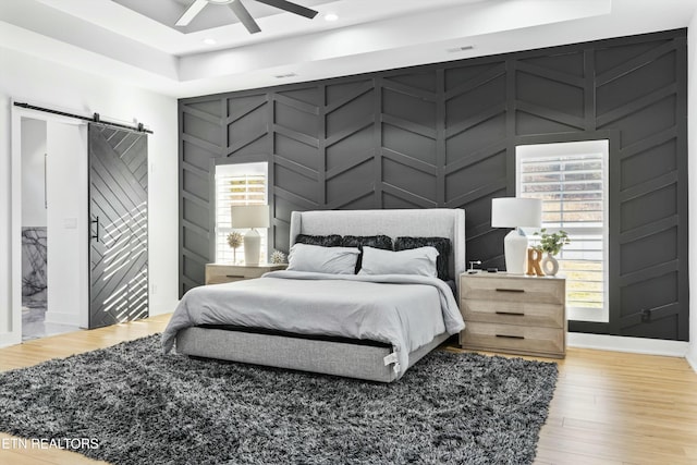 bedroom with light hardwood / wood-style flooring, ceiling fan, and a barn door