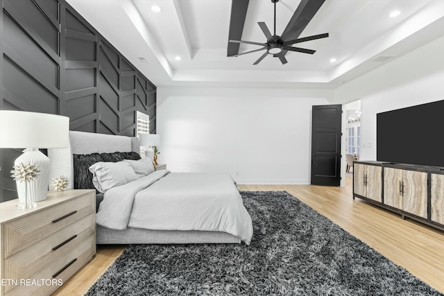 bedroom with ceiling fan, a raised ceiling, and light hardwood / wood-style floors