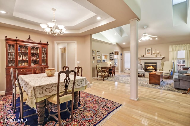 dining space featuring a tray ceiling, a warm lit fireplace, light wood-style flooring, and recessed lighting