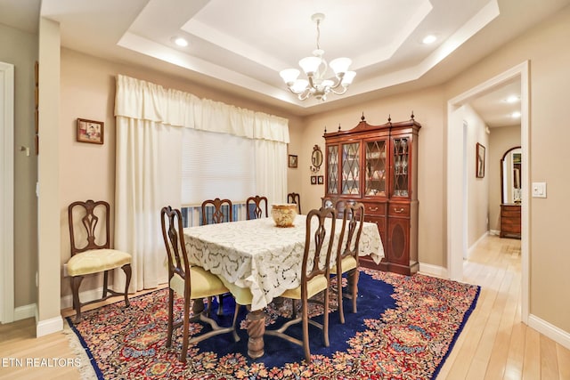 dining room featuring a chandelier, light wood finished floors, a raised ceiling, and baseboards