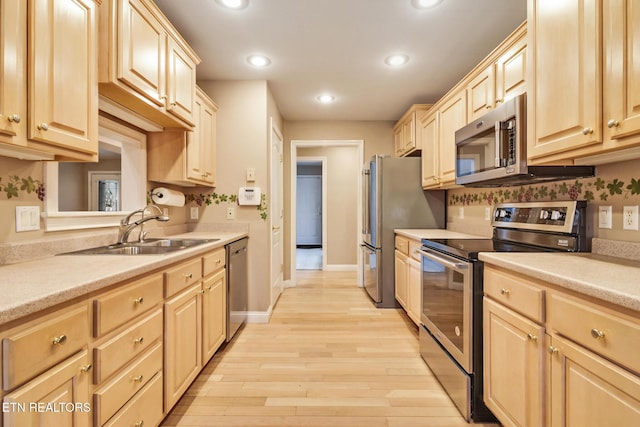 kitchen with light brown cabinets, stainless steel appliances, a sink, light wood-style floors, and light countertops