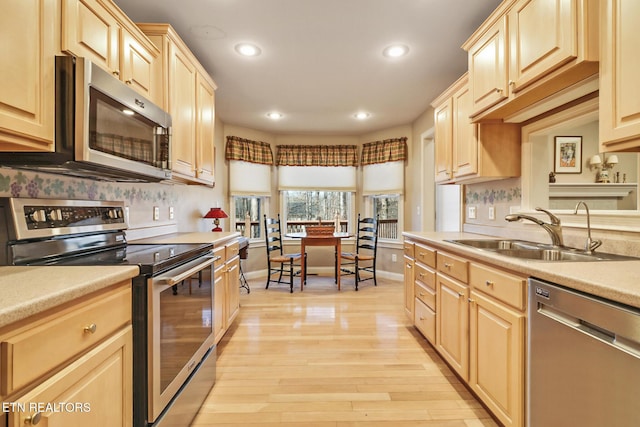 kitchen featuring appliances with stainless steel finishes, light countertops, a sink, and light brown cabinetry