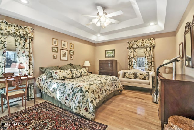 bedroom with light wood-style floors, a raised ceiling, and a ceiling fan