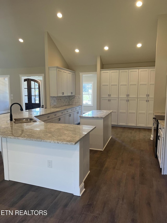 kitchen with kitchen peninsula, vaulted ceiling, dark hardwood / wood-style flooring, sink, and an island with sink