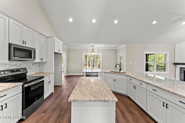 kitchen with stainless steel appliances, light stone countertops, white cabinets, a kitchen island, and sink