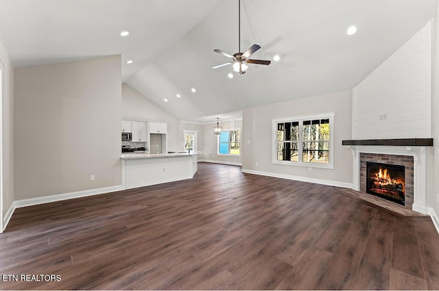 unfurnished living room with ceiling fan, high vaulted ceiling, dark wood-type flooring, and a fireplace