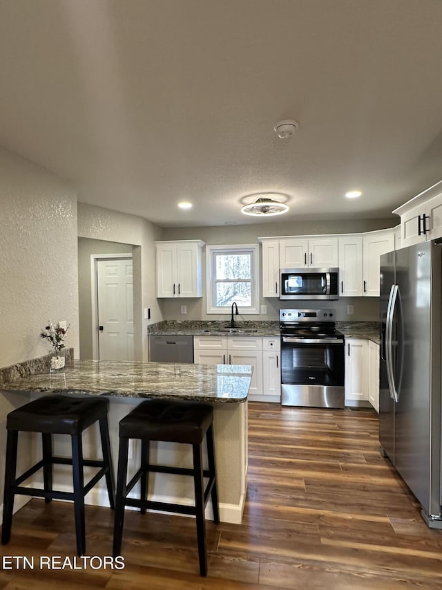 kitchen with a kitchen bar, white cabinetry, dark stone counters, kitchen peninsula, and stainless steel appliances