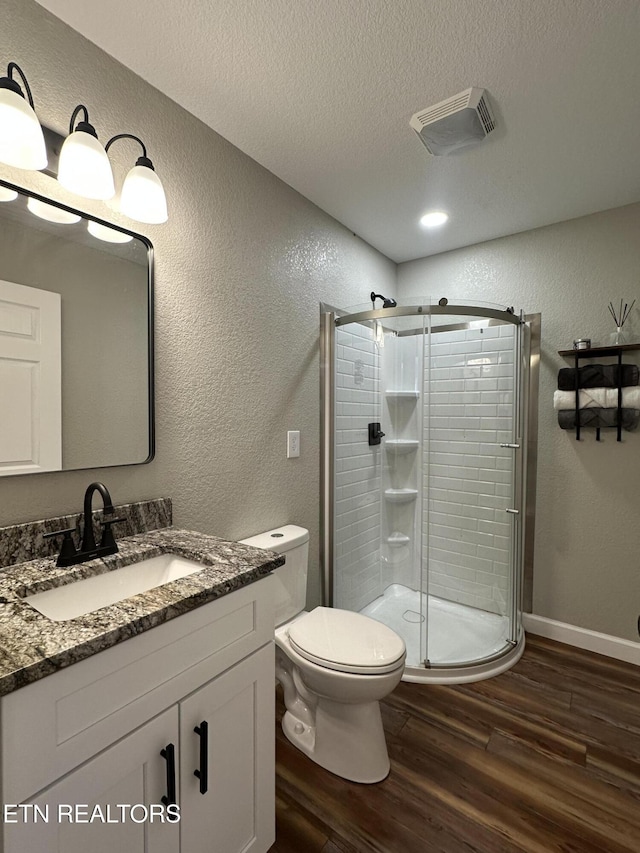 bathroom featuring hardwood / wood-style floors, vanity, toilet, a shower with door, and a textured ceiling