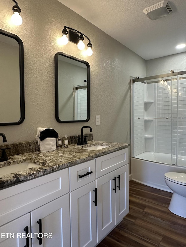 full bathroom featuring wood-type flooring, shower / bath combination with glass door, vanity, toilet, and a textured ceiling