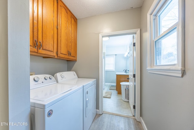 laundry area with cabinets, washing machine and clothes dryer, a textured ceiling, and light hardwood / wood-style flooring