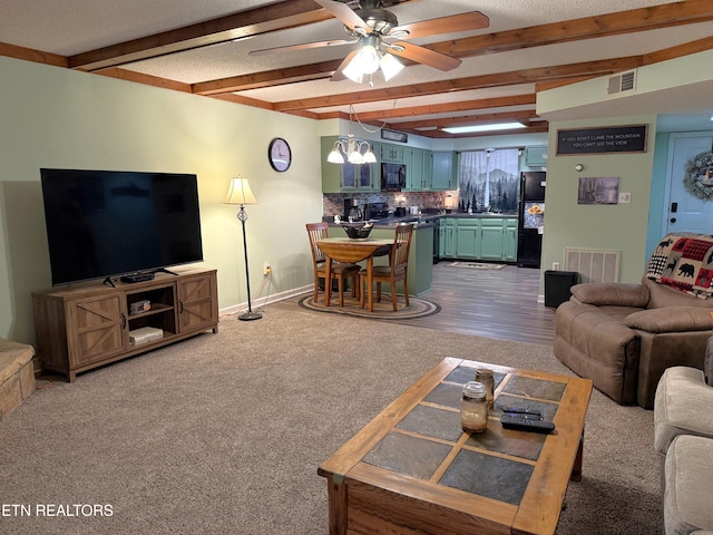 carpeted living room with ceiling fan and beamed ceiling