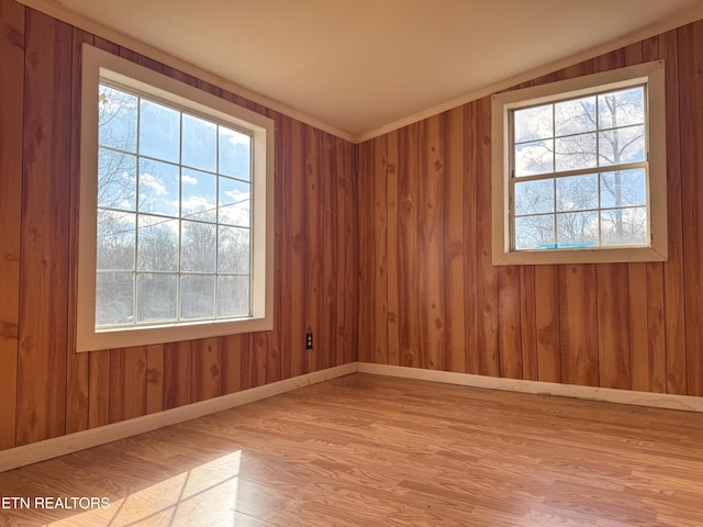 unfurnished room featuring plenty of natural light, light hardwood / wood-style floors, wood walls, and vaulted ceiling