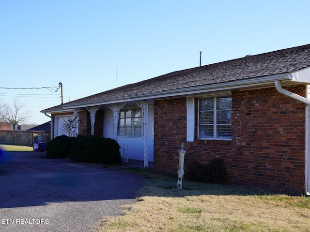 ranch-style home with an attached garage, aphalt driveway, brick siding, and a front yard