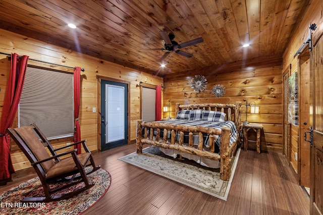 bedroom featuring ceiling fan, a barn door, wood walls, and dark hardwood / wood-style flooring