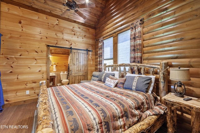 bedroom with hardwood / wood-style floors, rustic walls, ensuite bath, and a barn door