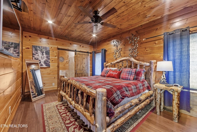 bedroom with ceiling fan, a barn door, hardwood / wood-style floors, and wooden walls