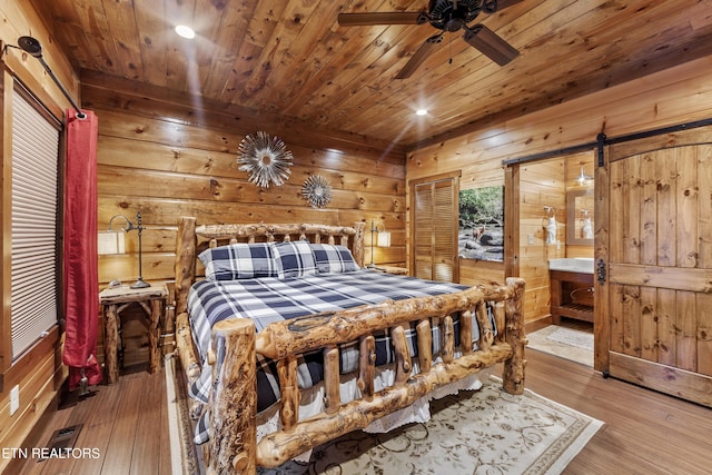 bedroom featuring wood-type flooring, ensuite bath, ceiling fan, and a barn door