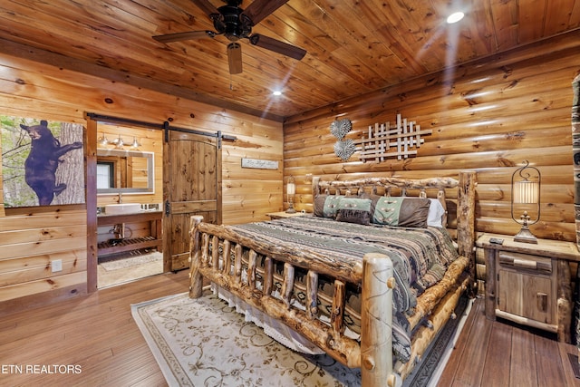 bedroom with wood-type flooring, rustic walls, ceiling fan, and a barn door