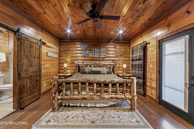 bedroom featuring a barn door, hardwood / wood-style floors, wooden ceiling, connected bathroom, and rustic walls