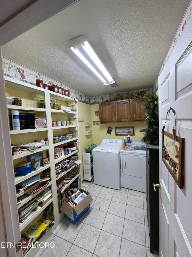 clothes washing area featuring cabinets, light tile patterned floors, a textured ceiling, and washing machine and clothes dryer