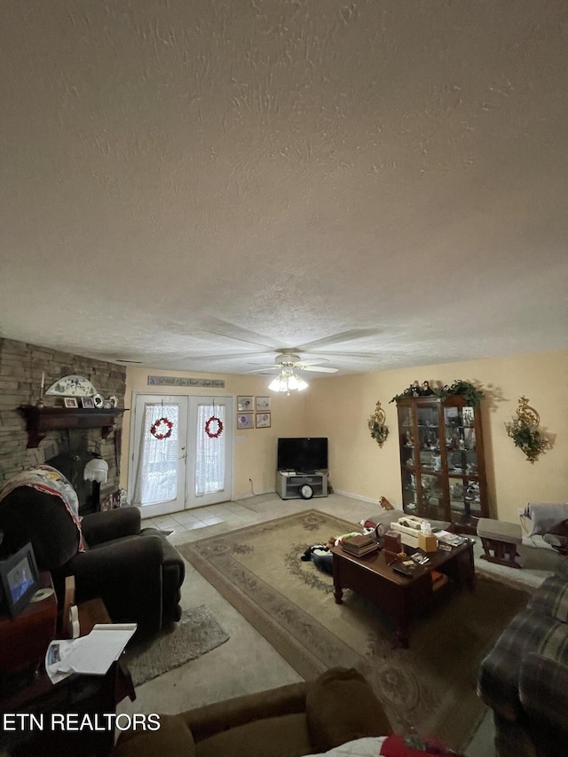 living room with french doors, ceiling fan, a stone fireplace, and a textured ceiling