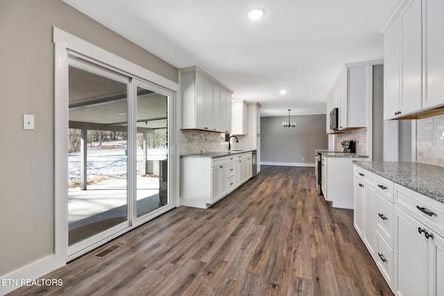 kitchen with white cabinetry, stainless steel appliances, decorative backsplash, sink, and hanging light fixtures