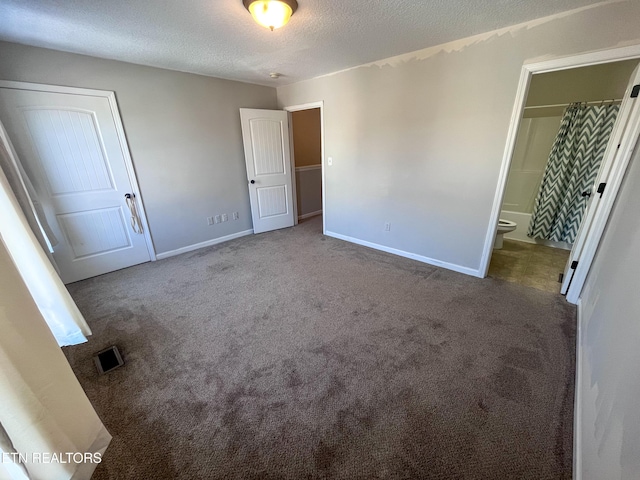 unfurnished bedroom featuring dark colored carpet, a textured ceiling, ensuite bath, and a closet