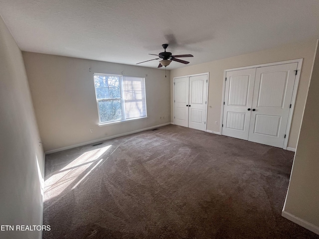 unfurnished bedroom featuring ceiling fan, dark carpet, and two closets