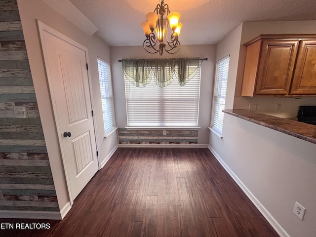 unfurnished dining area featuring dark hardwood / wood-style floors, a textured ceiling, and a notable chandelier