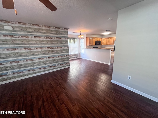 unfurnished living room with dark wood-type flooring, wooden walls, a textured ceiling, and ceiling fan with notable chandelier