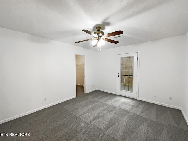 spare room featuring ceiling fan, dark carpet, and a textured ceiling