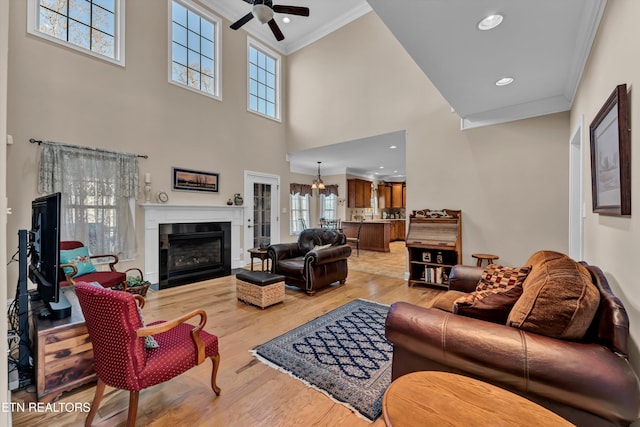 living room with crown molding, ceiling fan with notable chandelier, light hardwood / wood-style floors, and a high ceiling