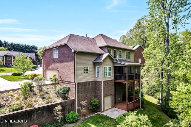 rear view of property with a garage, brick siding, and a sunroom