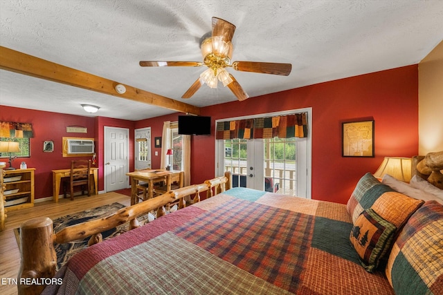 bedroom with an AC wall unit, hardwood / wood-style flooring, access to exterior, ceiling fan, and a textured ceiling