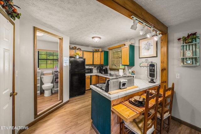 kitchen with a breakfast bar area, tile countertops, black refrigerator, track lighting, and kitchen peninsula