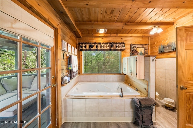 bathroom with wood ceiling, wooden walls, tiled tub, beam ceiling, and hardwood / wood-style floors