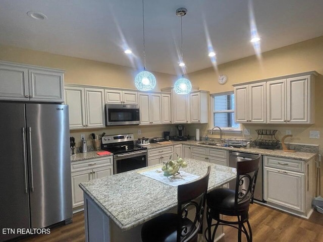 kitchen featuring a center island, sink, pendant lighting, stainless steel appliances, and light stone counters