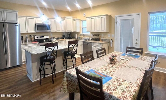 kitchen with hanging light fixtures, appliances with stainless steel finishes, light stone counters, dark hardwood / wood-style floors, and a kitchen island