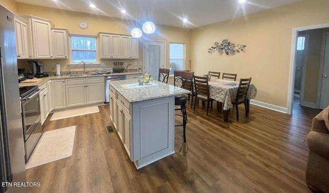 kitchen with appliances with stainless steel finishes, hanging light fixtures, sink, a kitchen island, and a breakfast bar area