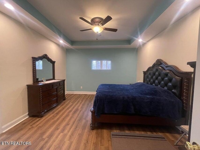 bedroom featuring ceiling fan, wood-type flooring, and a tray ceiling