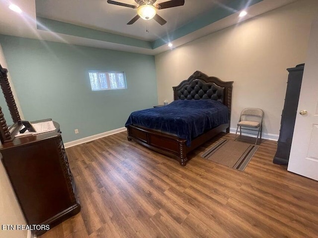 bedroom with ceiling fan, dark hardwood / wood-style floors, and a tray ceiling