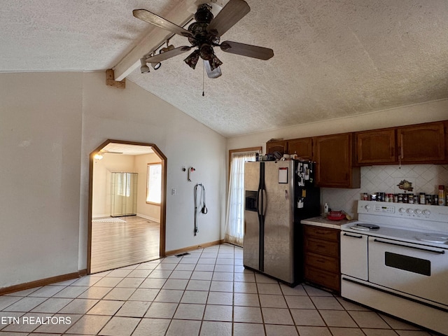 kitchen with light tile patterned floors, stainless steel fridge, backsplash, white electric range oven, and lofted ceiling with beams