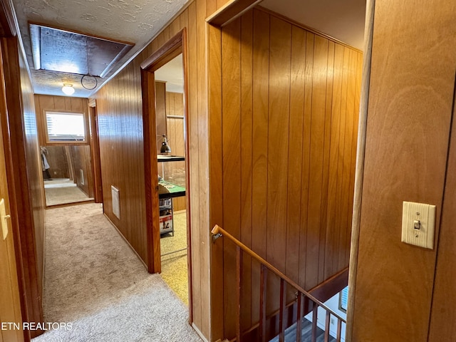 hall featuring light colored carpet, a textured ceiling, and wood walls