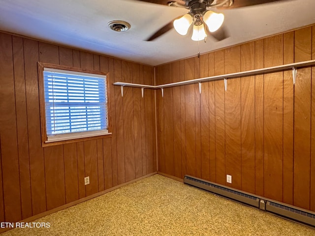 spare room with a baseboard heating unit, ceiling fan, and wood walls