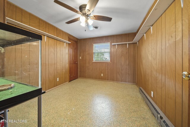 interior space with ceiling fan, baseboard heating, and wood walls