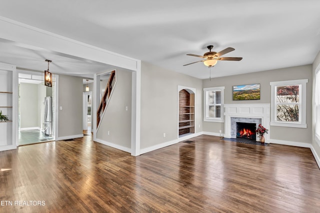 unfurnished living room with dark hardwood / wood-style flooring, ceiling fan with notable chandelier, and built in features