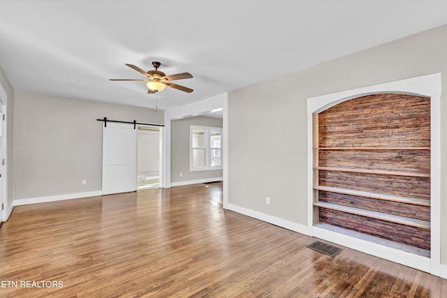 unfurnished room with wood-type flooring, a barn door, and ceiling fan