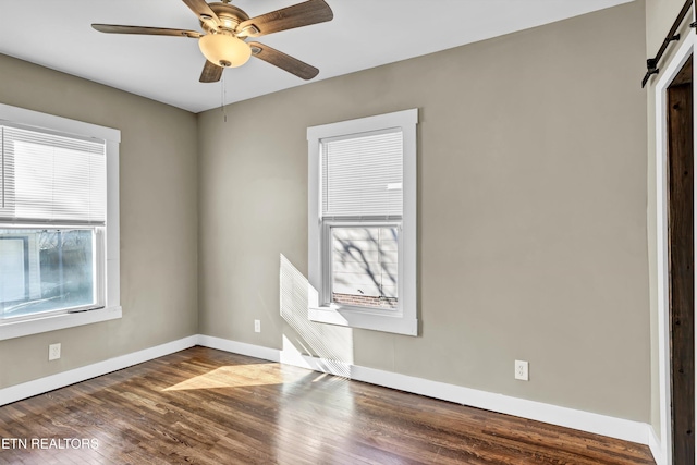 empty room with dark hardwood / wood-style flooring, a barn door, and ceiling fan