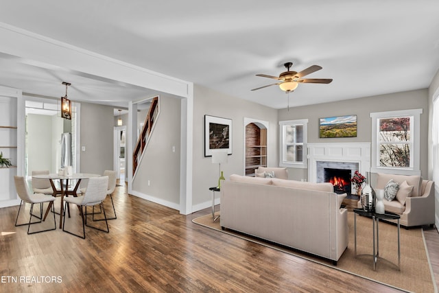 living room featuring dark hardwood / wood-style flooring, ceiling fan with notable chandelier, a fireplace, and built in features