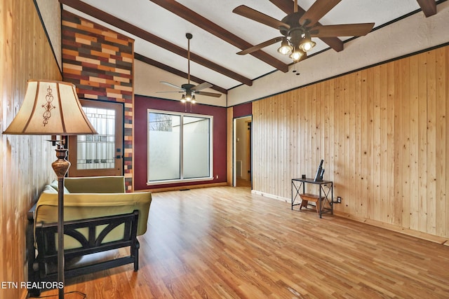 sitting room with ceiling fan, beam ceiling, hardwood / wood-style floors, and wood walls